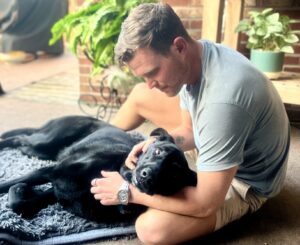 Logan holding Clydey, a black dog, in his arms